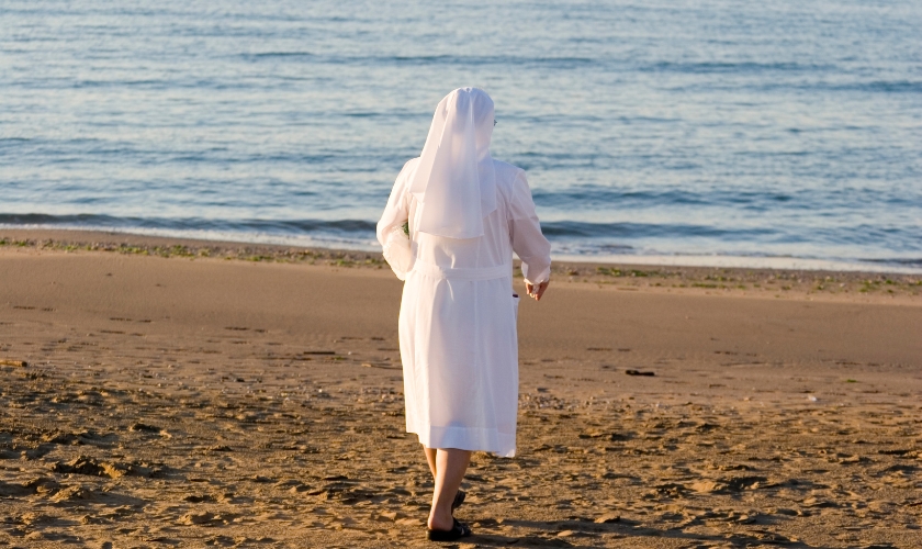 Ordensschwester geht auf einem Strand Richtung Meer
